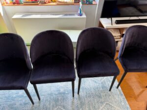 Four dark upholstered chairs are arranged side-by-side in front of a window and radiator.