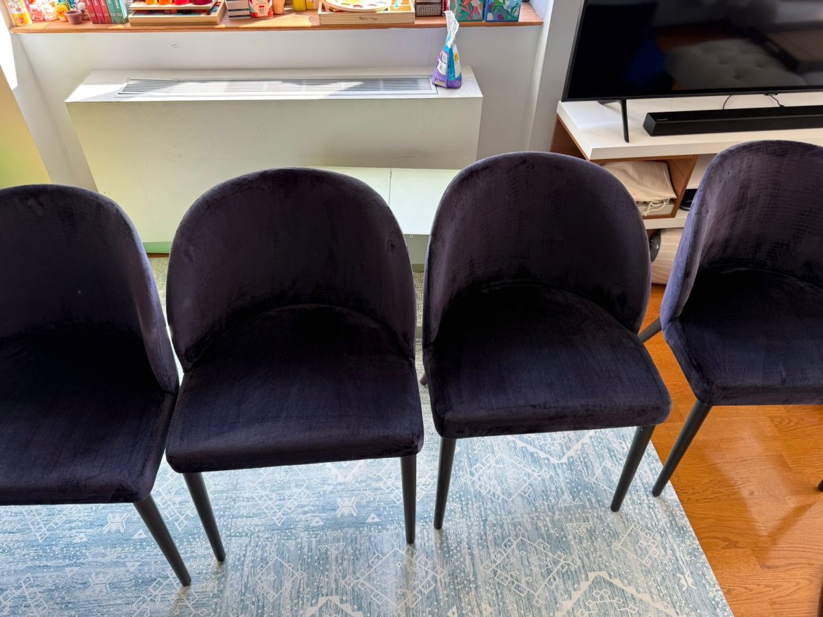 Four dark upholstered chairs are arranged side-by-side in front of a window and radiator.